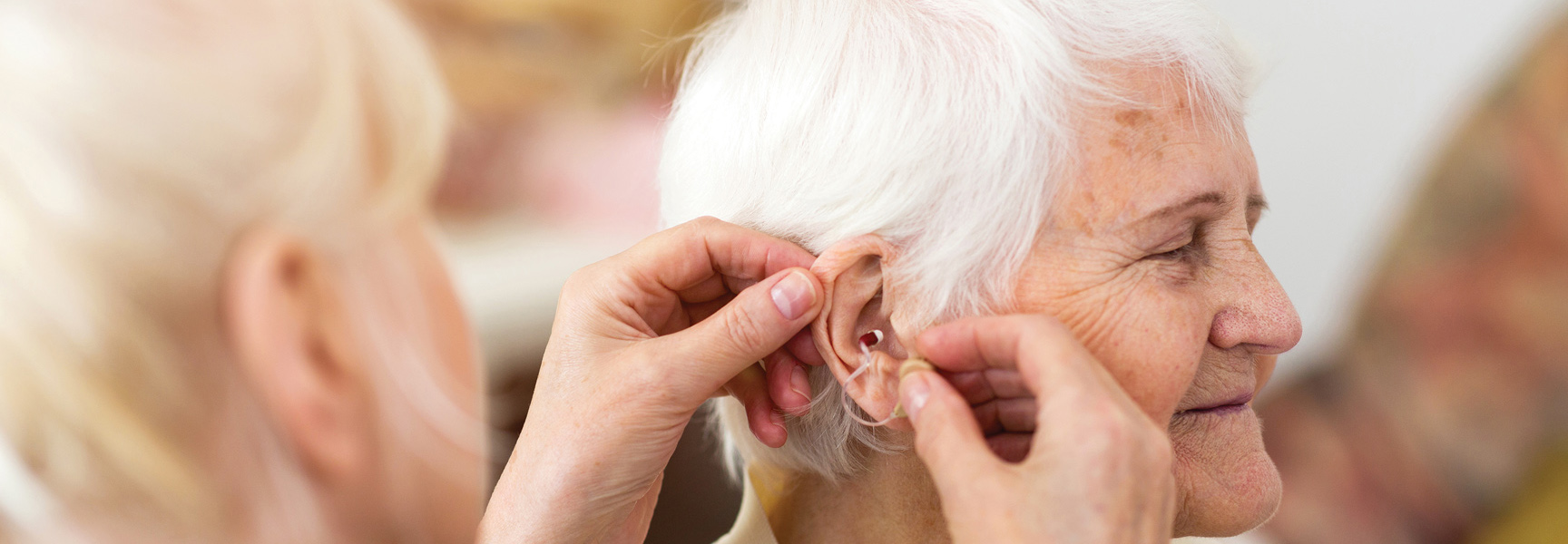 A close-up of an older woman with white hair being fitted for a hearing aid.