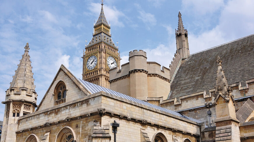 The iconic Big Ben clock tower and the ornate Gothic buildings of the Palace of Westminster under a blue sky in London, England.