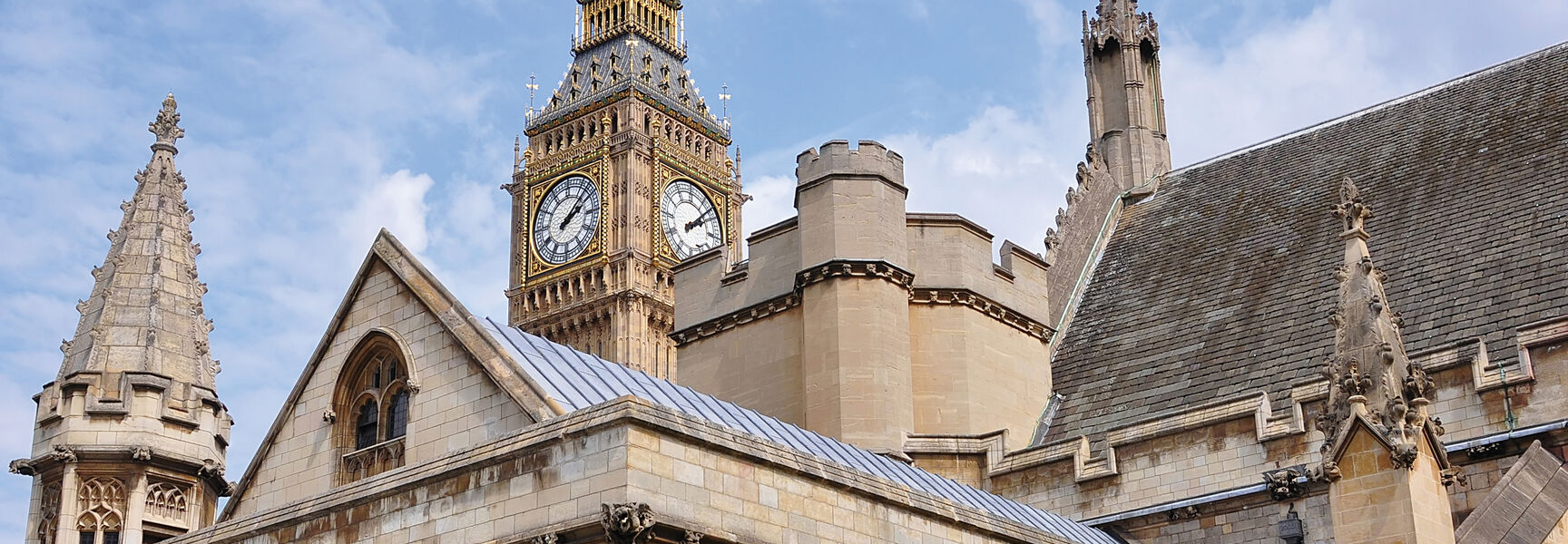 The iconic Big Ben clock tower and the ornate Gothic buildings of the Palace of Westminster under a blue sky in London, England.