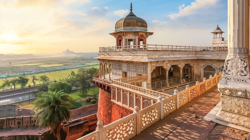 Ornate marble architecture at Agra Fort in India overlooking a hazy landscape with the Taj Mahal in the distance, showcasing the country's royal heritage.