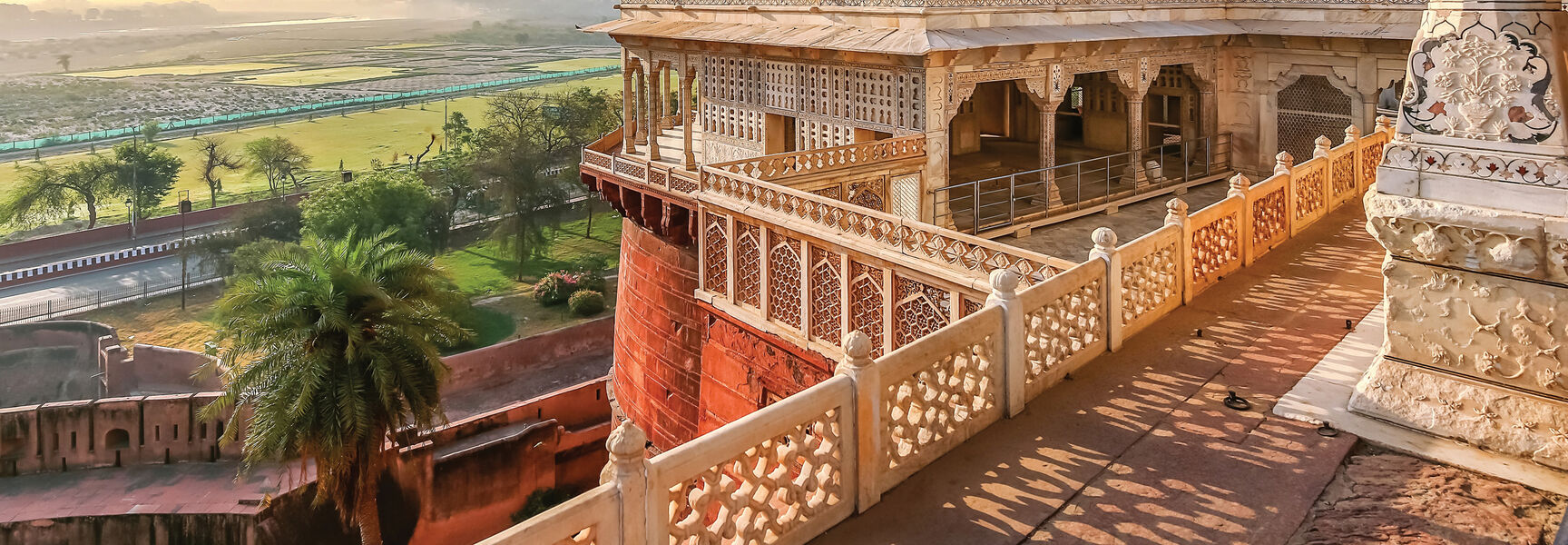 Ornate marble architecture at Agra Fort in India overlooking a hazy landscape with the Taj Mahal in the distance, showcasing the country's royal heritage.