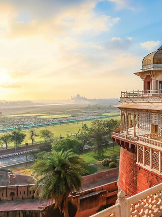 Ornate marble architecture at Agra Fort in India overlooking a hazy landscape with the Taj Mahal in the distance, showcasing the country's royal heritage.