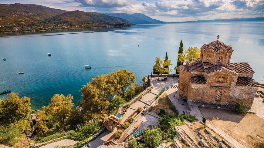 A historic stone church overlooks a vast lake and the Julian Alps, showcasing the rich cultural heritage and natural wonders of Slovenia and Croatia.