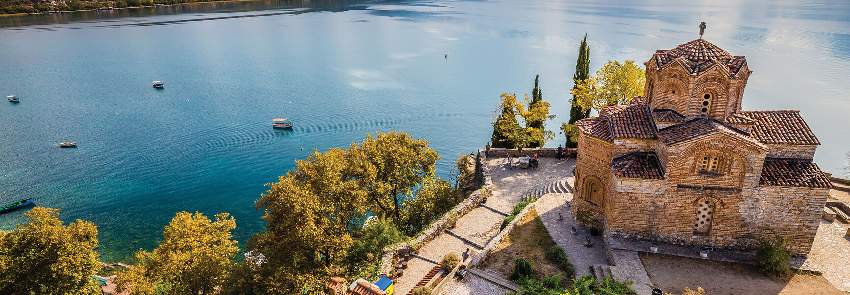 A historic stone church overlooks a vast lake and the Julian Alps, showcasing the rich cultural heritage and natural wonders of Slovenia and Croatia.