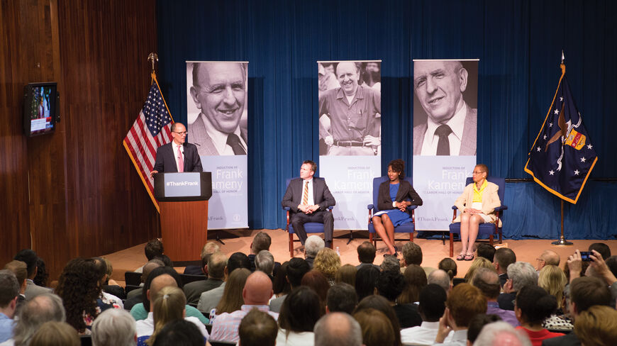 A speaker addresses an audience during the induction of Frank Kameny into the Labor Hall of Honor, featuring large banners of the activist.