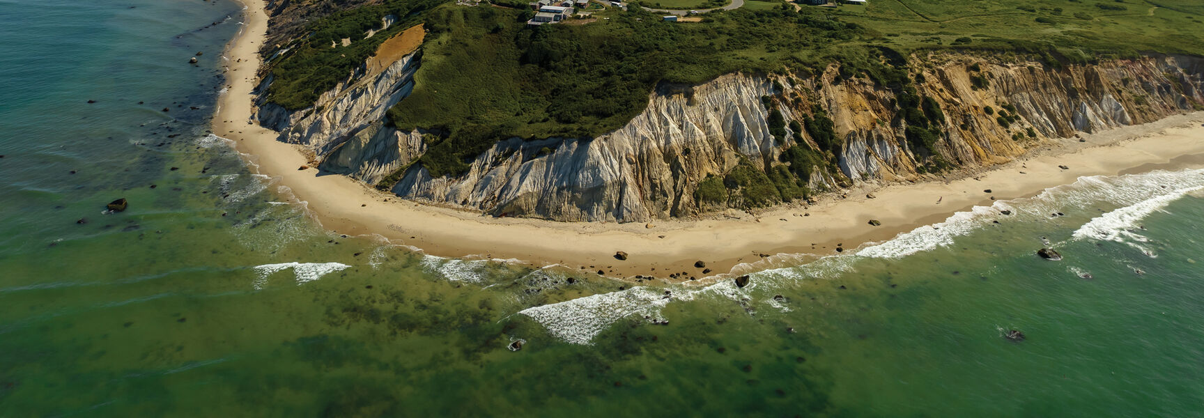 Aerial view of the iconic Gay Head Cliffs on Martha’s Vineyard, featuring colorful clay bluffs, a sandy beach, and clear coastal New England waters.