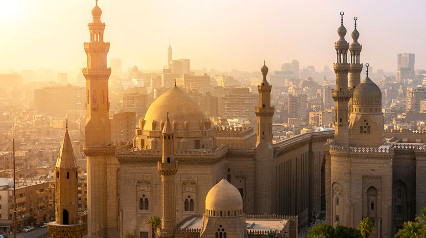 The domes and minarets of several mosques rise above the sprawling cityscape of Cairo at sunset.