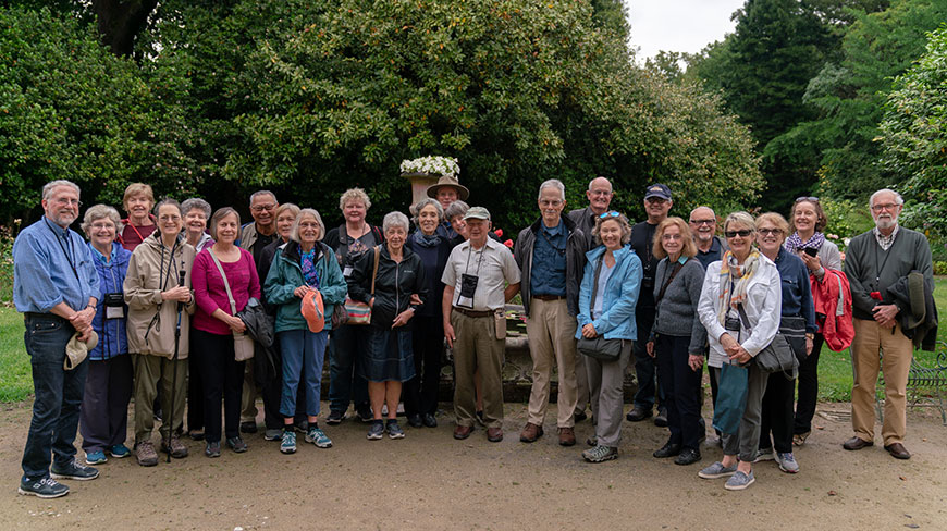 A large group of travelers poses for a photo in a lush, green garden.