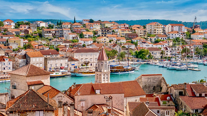 A scenic view of the historic town of Trogir, Croatia, with its red-roofed buildings surrounding a bustling harbor filled with boats.