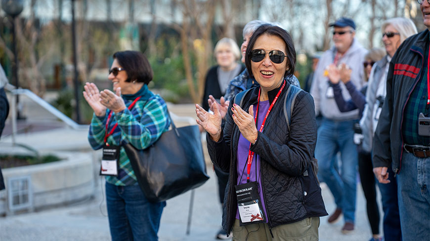 A smiling woman wearing sunglasses and a group of people clap while participating in a downtown walking tour in Los Angeles.