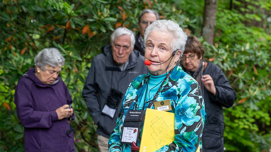 A volunteer guide leads a group tour through the lush green foliage at the Pittock Mansion in Portland, Oregon.