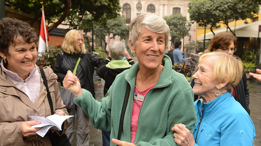 A group of women smile and interact while standing together outdoors in a city plaza.