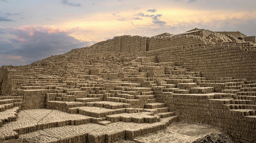 The ancient adobe brick pyramid of Huaca Pucllana in Lima, Peru, stands against a colorful sunset sky.