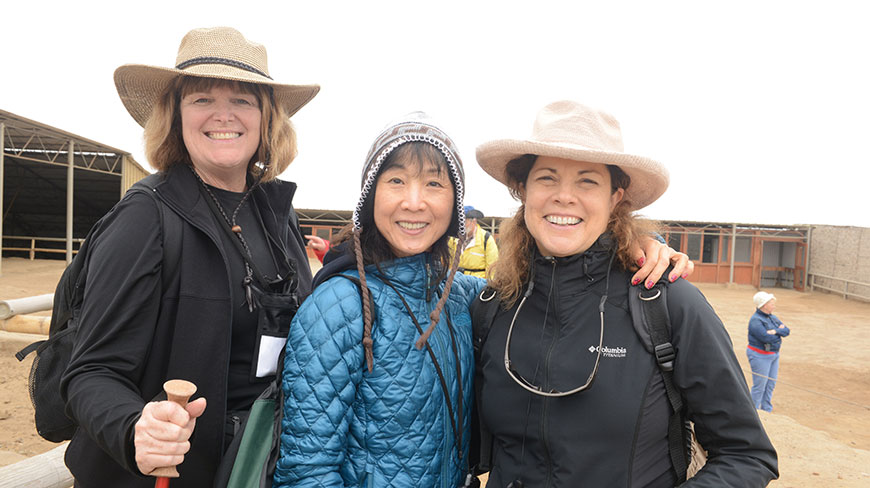 Three women in hats and jackets smile together for a photo while on a trip outdoors.