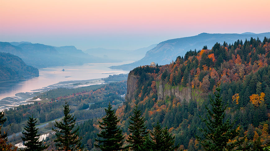 Sunset over the Columbia River Gorge in Oregon featuring Vista House atop a cliff overlooking the river and autumn-colored forests.