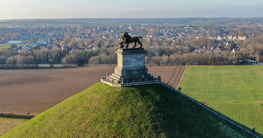 The Lion’s Mound in Waterloo, Belgium, features a lion statue atop a large conical grass hill overlooking the surrounding fields and town.