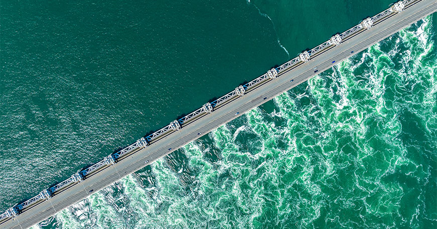 Aerial view of a Delta Works dam in the Netherlands with turquoise water rushing through the gates and cars driving along the top.