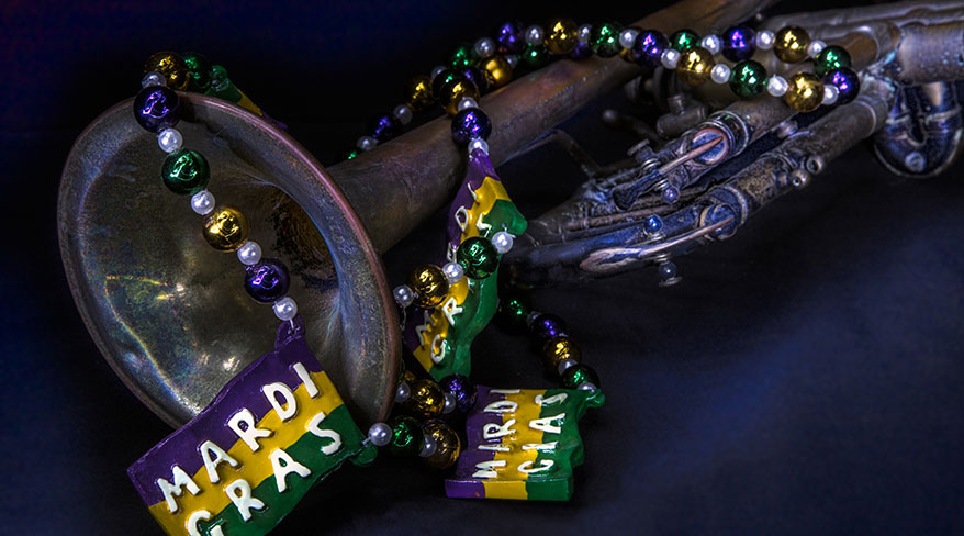 A brass jazz trumpet adorned with colorful purple, green, and gold Mardi Gras beads and signs in New Orleans.