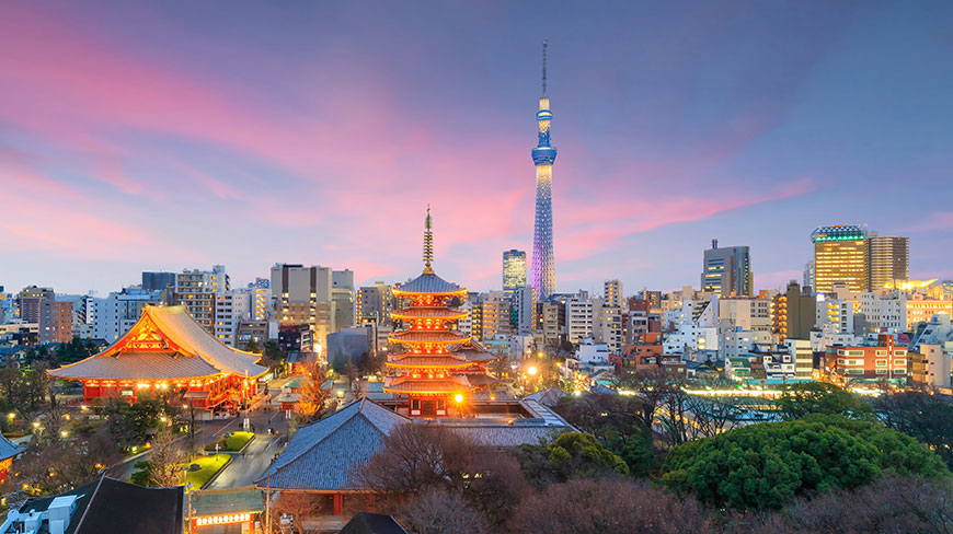 The Tokyo skyline at sunset, with the illuminated Senso-ji Temple in the foreground and the Tokyo Skytree against a colorful sky.