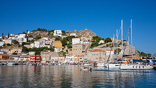 Sailboats and other boats in the harbor of a picturesque hillside town on the Greek island of Hydra.