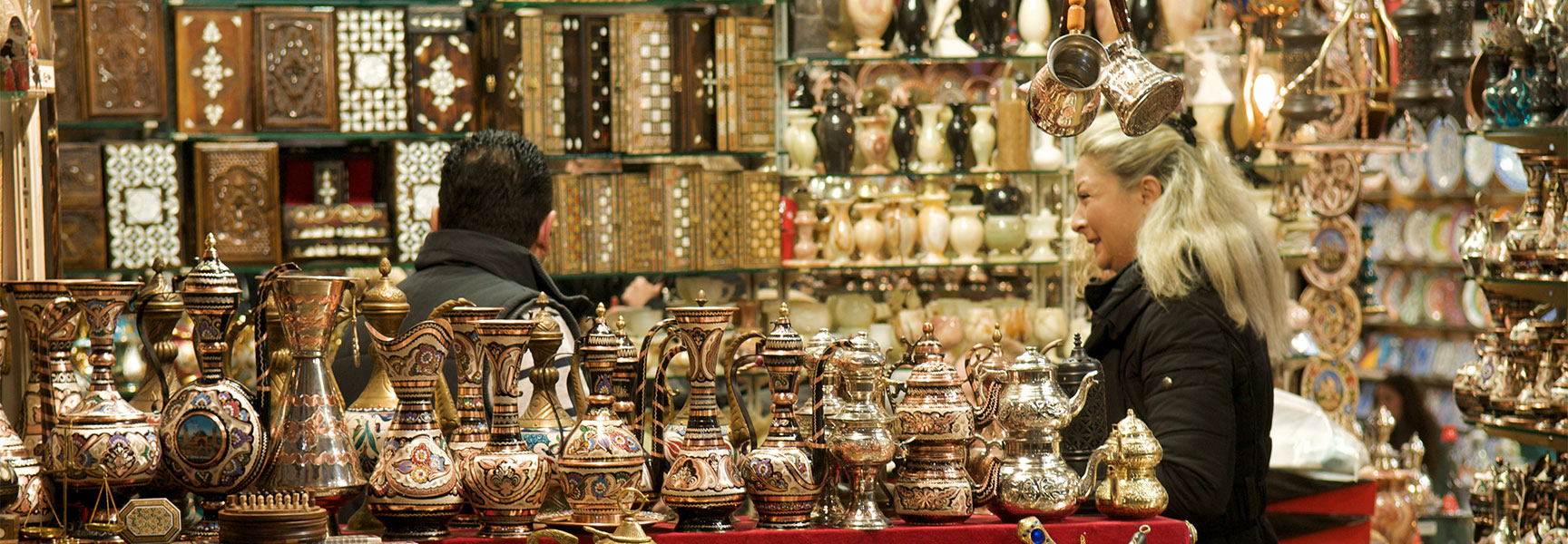 A woman browses a stall filled with ornate metal lamps and handcrafted boxes in the Istanbul Grand Bazaar.