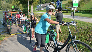 Cyclists wearing helmets push their bikes along a paved path in Schlogen during a biking trip along the Danube River.