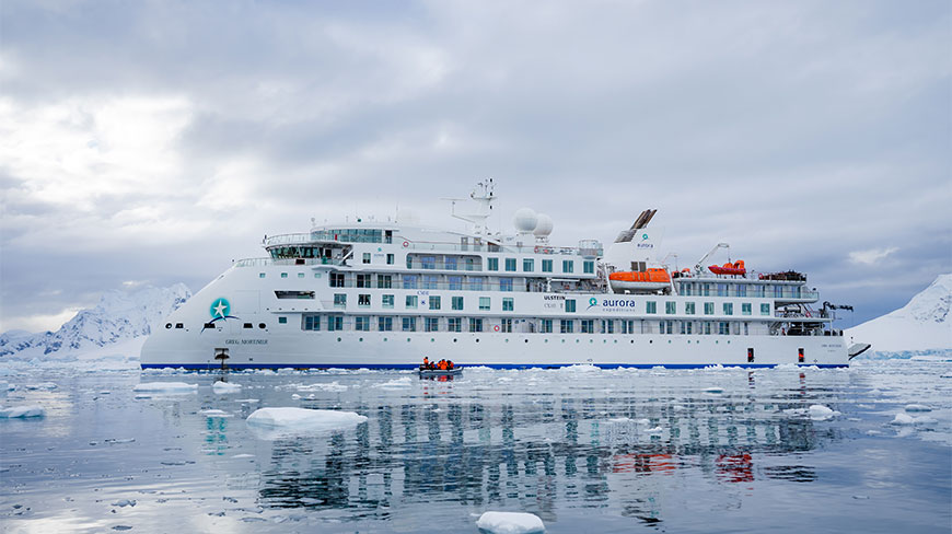 The Greg Mortimer cruise ship sits in the icy waters of Paradise Bay, surrounded by small icebergs and snow-covered mountains.