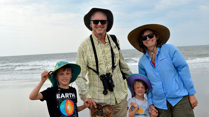 Participants on an Ocean Science Adventure at Wallops Island, Virginia, smile on the beach while holding a prehistoric horseshoe crab with their grandchildren.