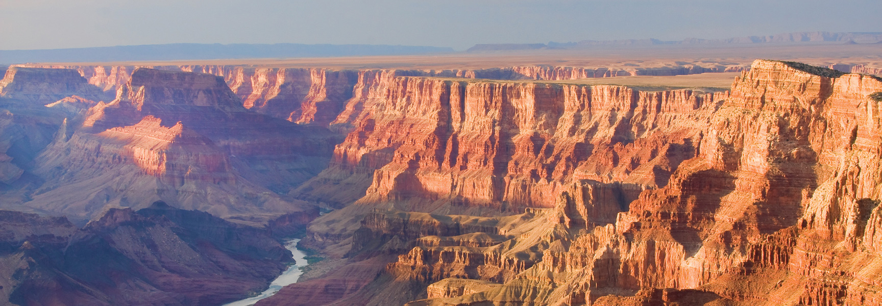 The sun sets over the Grand Canyon in Arizona, casting a warm glow on the red rock formations and the Colorado River below.