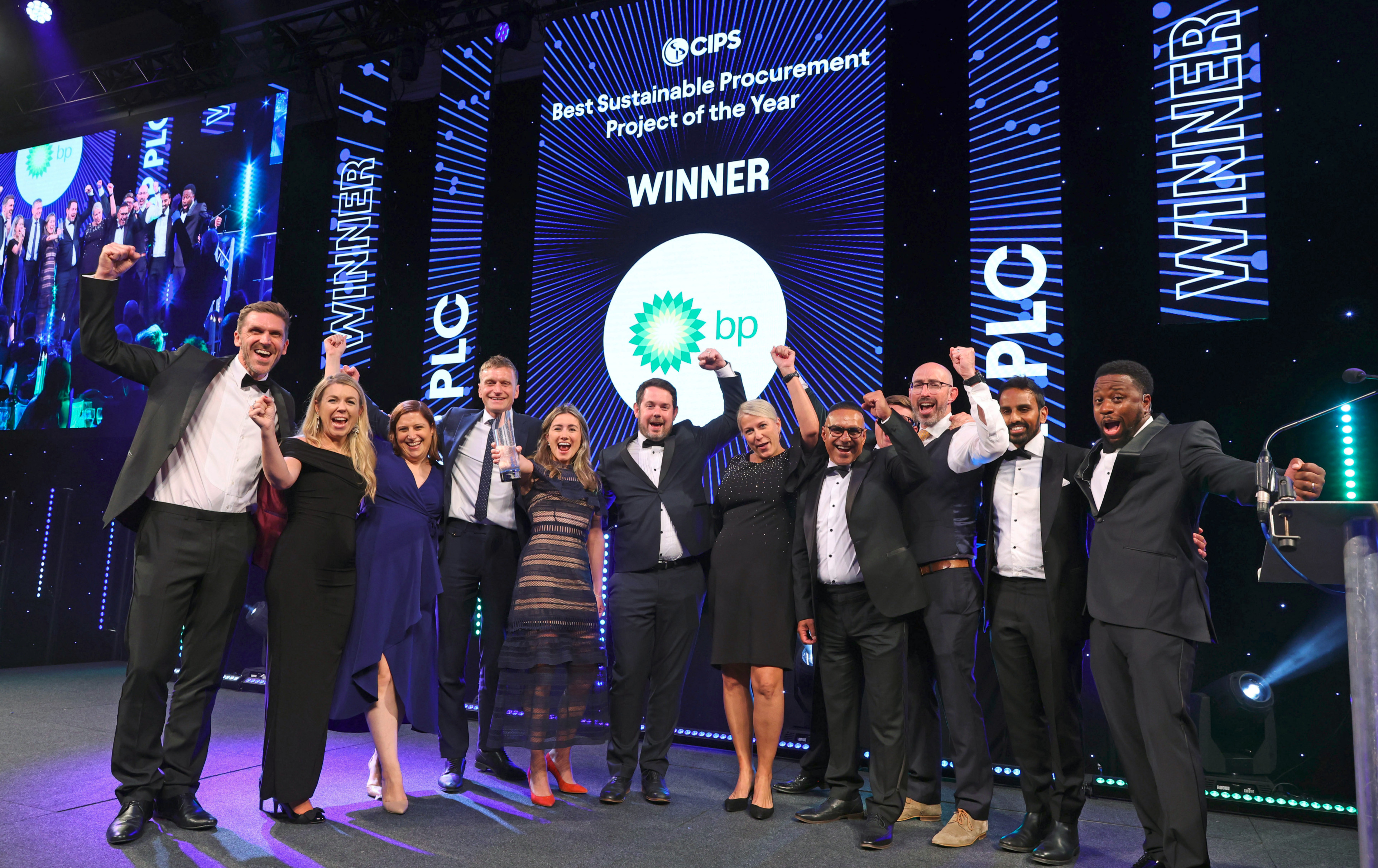 Group of 11 people, dressed in black tie, cheering on a stage. Sign in background says 'CIPS Best sustainable procurement project of the year' Winner BP