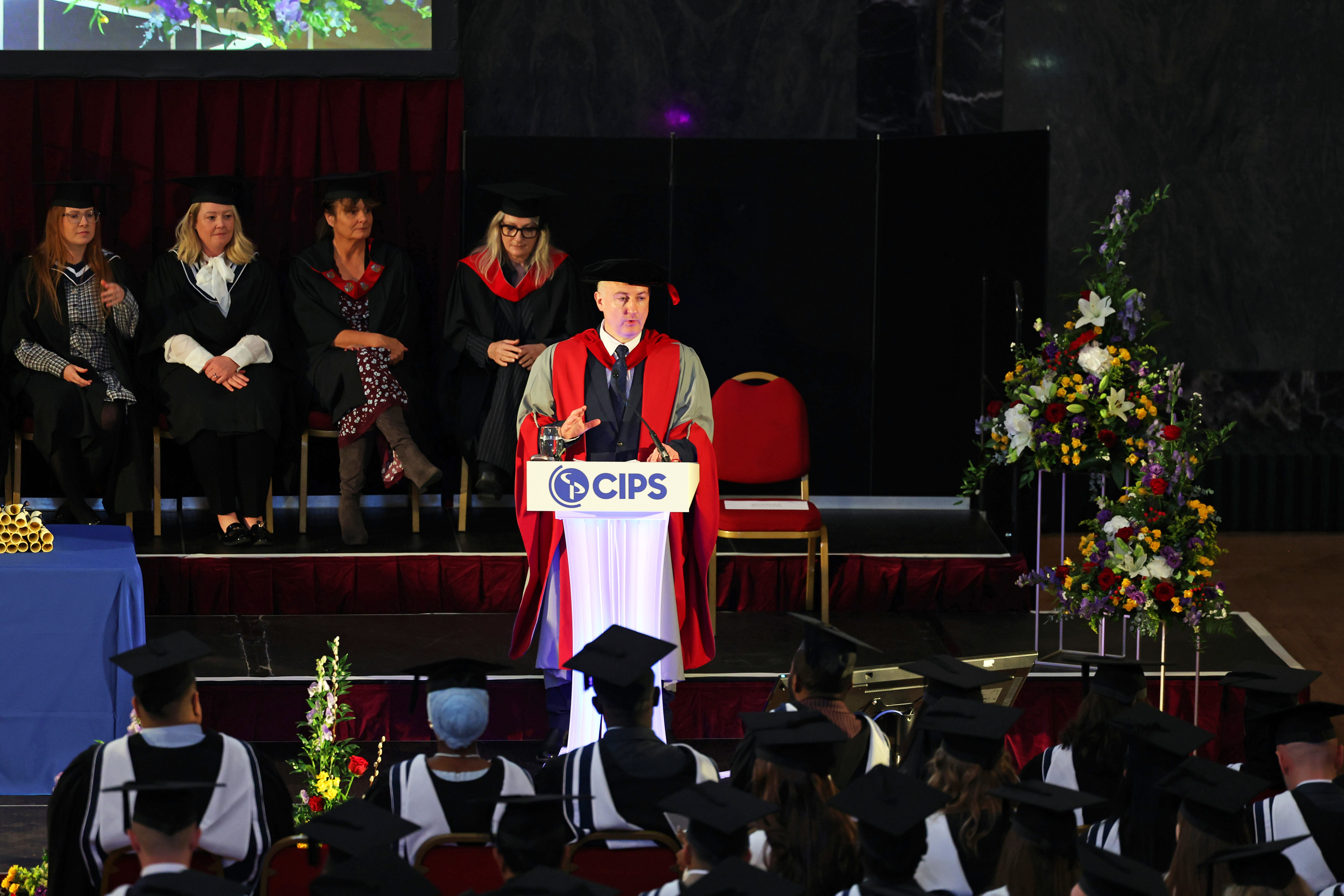 Male speaker dressed in academic robes, at a CIPS branded podium addressing a graduation audience.