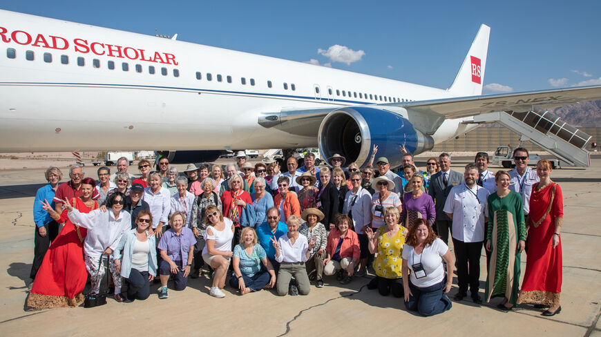 A large Road Scholar group poses for a photo in front of a private plane on an airport tarmac.