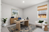 bedroom styled as an office with light wood desk, blue desk chair, light gray carpet, and window