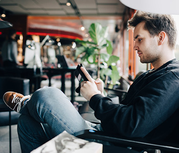 Mlad moški sedi v kavarni in uporablja mobilni telefon - trenutno ni videti, da bi imel težave