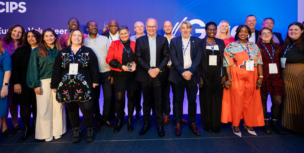 Group of 19 different CIPS volunteers, standing on a stage together, with Ben Farrell, CIPS CEO, in the center of the group