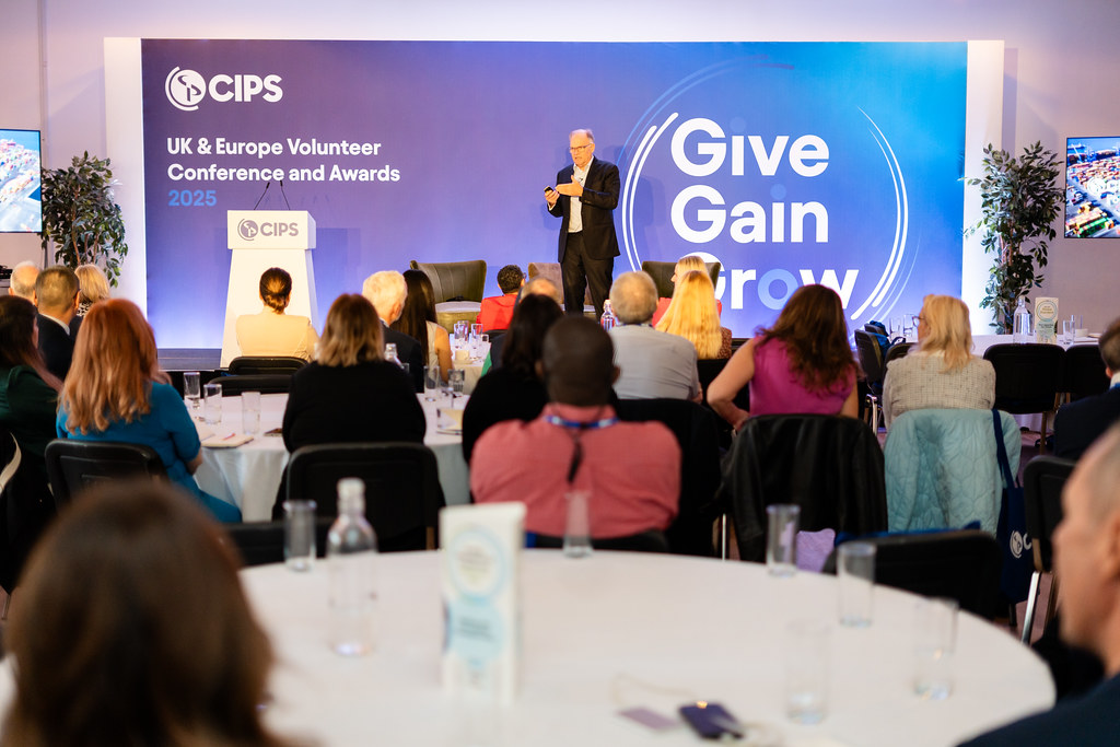 Ben Farrell, CIPS CEO, on a stage, giving presentation to group of people seated at tables