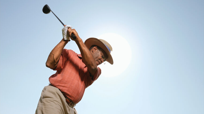 A man in a straw hat swings a golf club on a sunny Utah golf course during an expert instruction session.