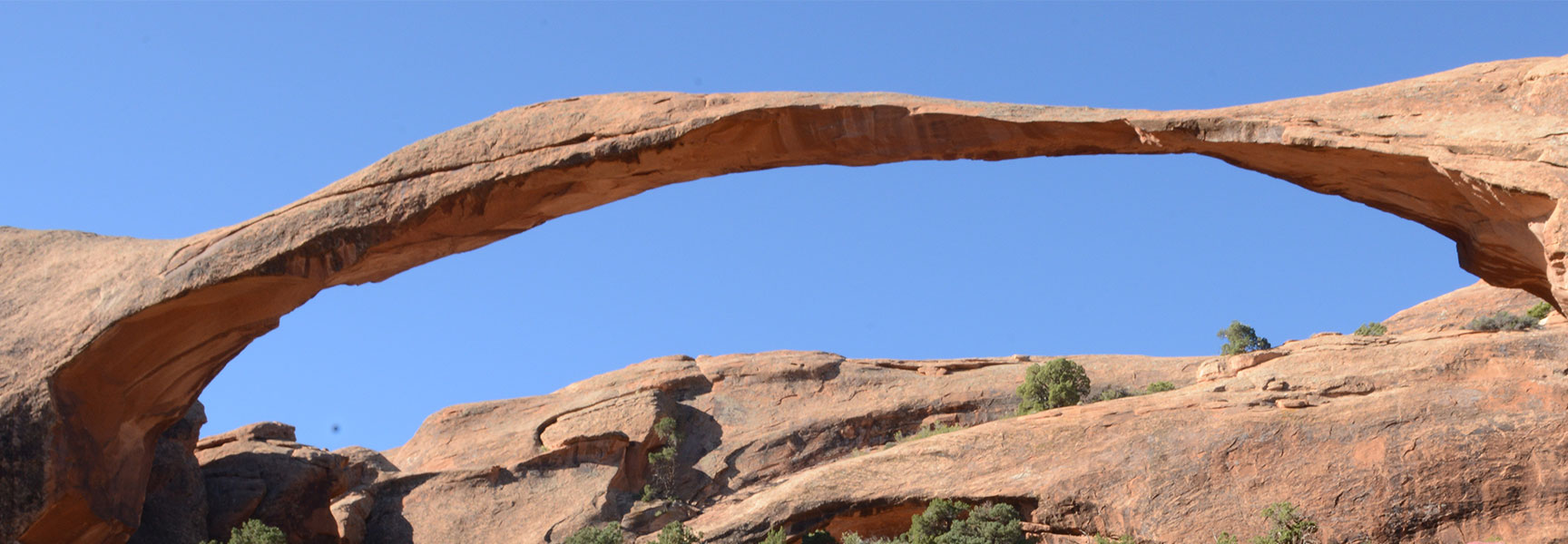 The long and slender Landscape Arch stretches against a clear blue sky in Arches National Park, Utah.