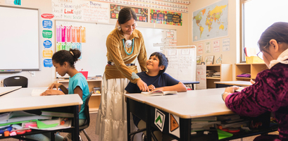 A Navajo teacher in traditional attire helps a student with their schoolwork in a classroom on the Navajo Reservation in Arizona.