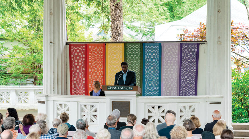 A speaker delivers a lecture on foreign policy at the Chautauqua Institution in New York before an audience seated in an open-air pavilion.