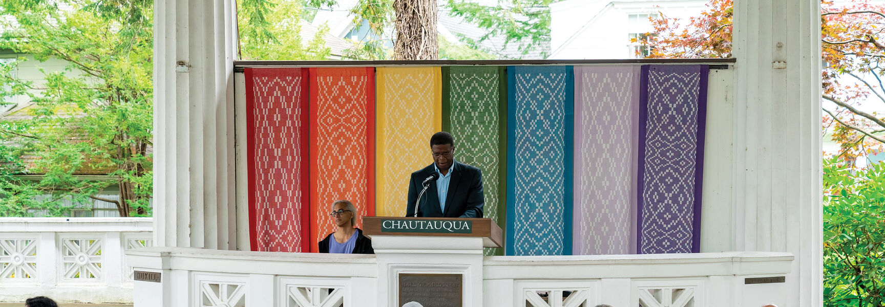 A speaker delivers a lecture on foreign policy at the Chautauqua Institution in New York before an audience seated in an open-air pavilion.