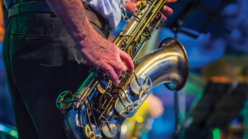 A musician wearing red suspenders plays a brass saxophone during a performance at Monterey's Jazz Bash by the Bay in California.