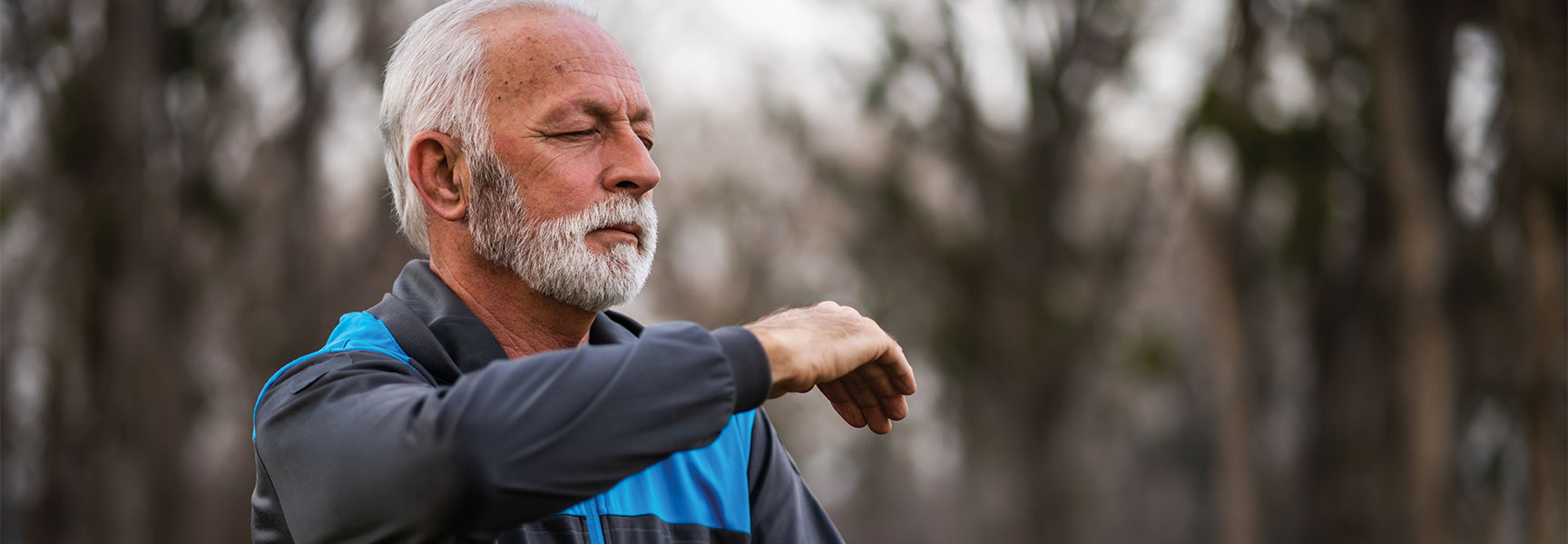 An older man with a white beard and closed eyes practices Qi Gong outdoors in a California park.