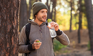 Zdrav življenjski slog je odličen način za krepitev imunskega sistema, mlad moški zato uživa požirek čiste vode na sprehodu v naravi.