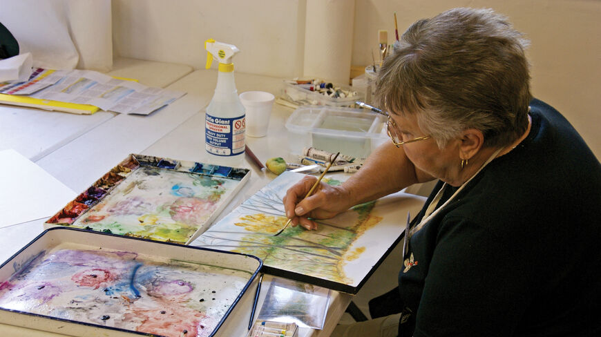 A woman paints a watercolor landscape on Jekyll Island, Georgia, surrounded by paint trays and brushes during an art workshop.