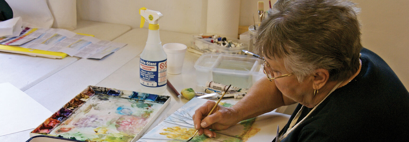A woman paints a watercolor landscape on Jekyll Island, Georgia, surrounded by paint trays and brushes during an art workshop.