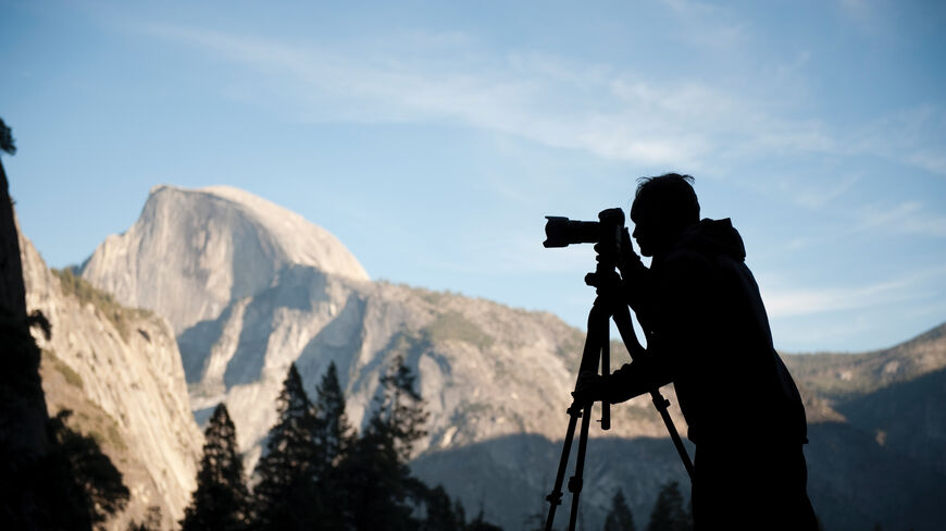 Silhouette of a photographer with a tripod-mounted camera capturing Half Dome in Yosemite National Park, California.