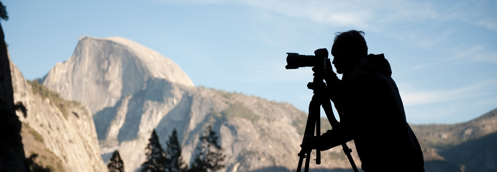 A silhouette of a photographer with a camera on a tripod captures the view of Half Dome in Yosemite National Park, California.
