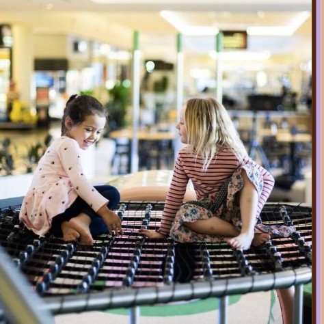 A picture of two kids sitting on top of a playground located inside Canberra Centre 