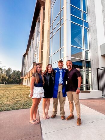 A family poses in front of the school with their son wearing a blue lab coat.